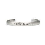 Satin brushed sterling silver cuff bracelet with champagne diamonds next to custom engraving reading "C'est la vie" in fine Gothic letters