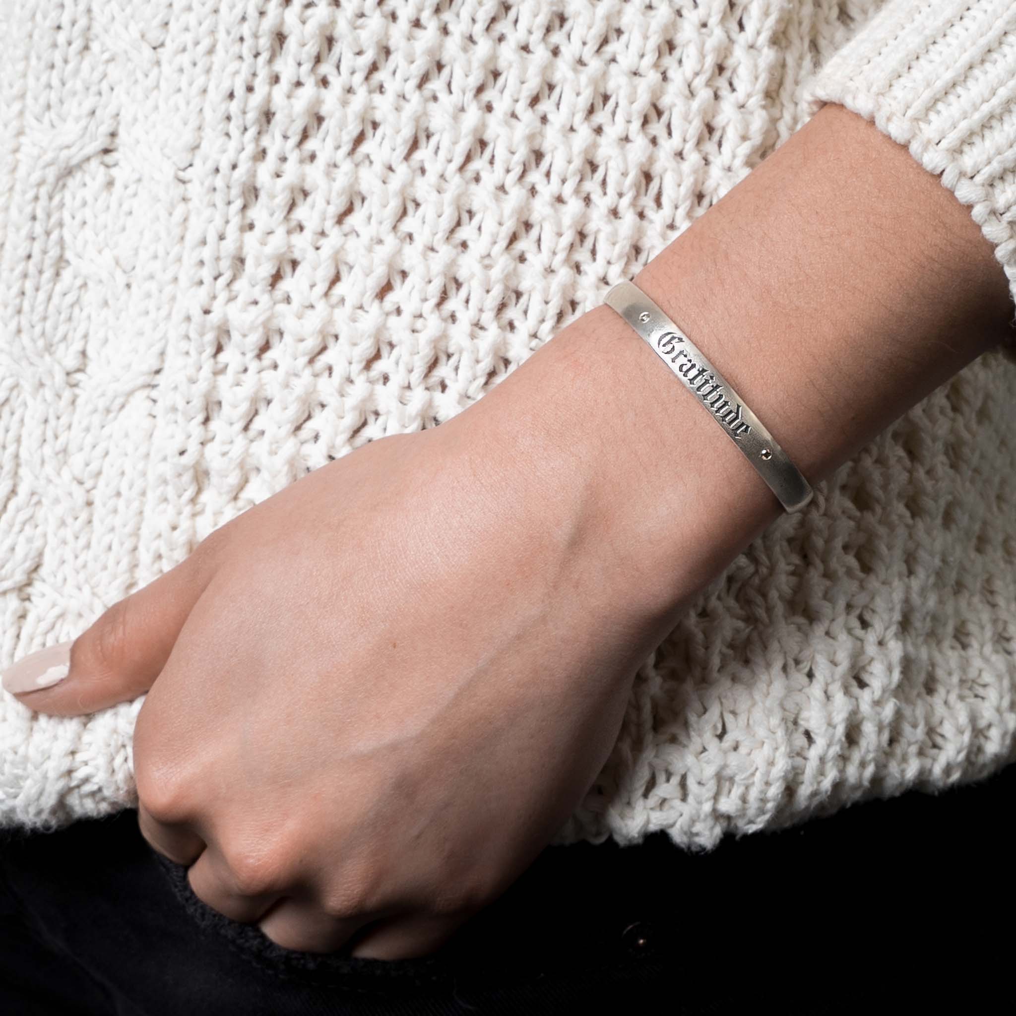Sterling silver cuff with "Gratitude" engraved on it pictured on a woman's wrist