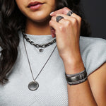 Closeup of a woman wearing three sterling silver layering necklaces and showing a stack of darkened silver cuffs on her wrist